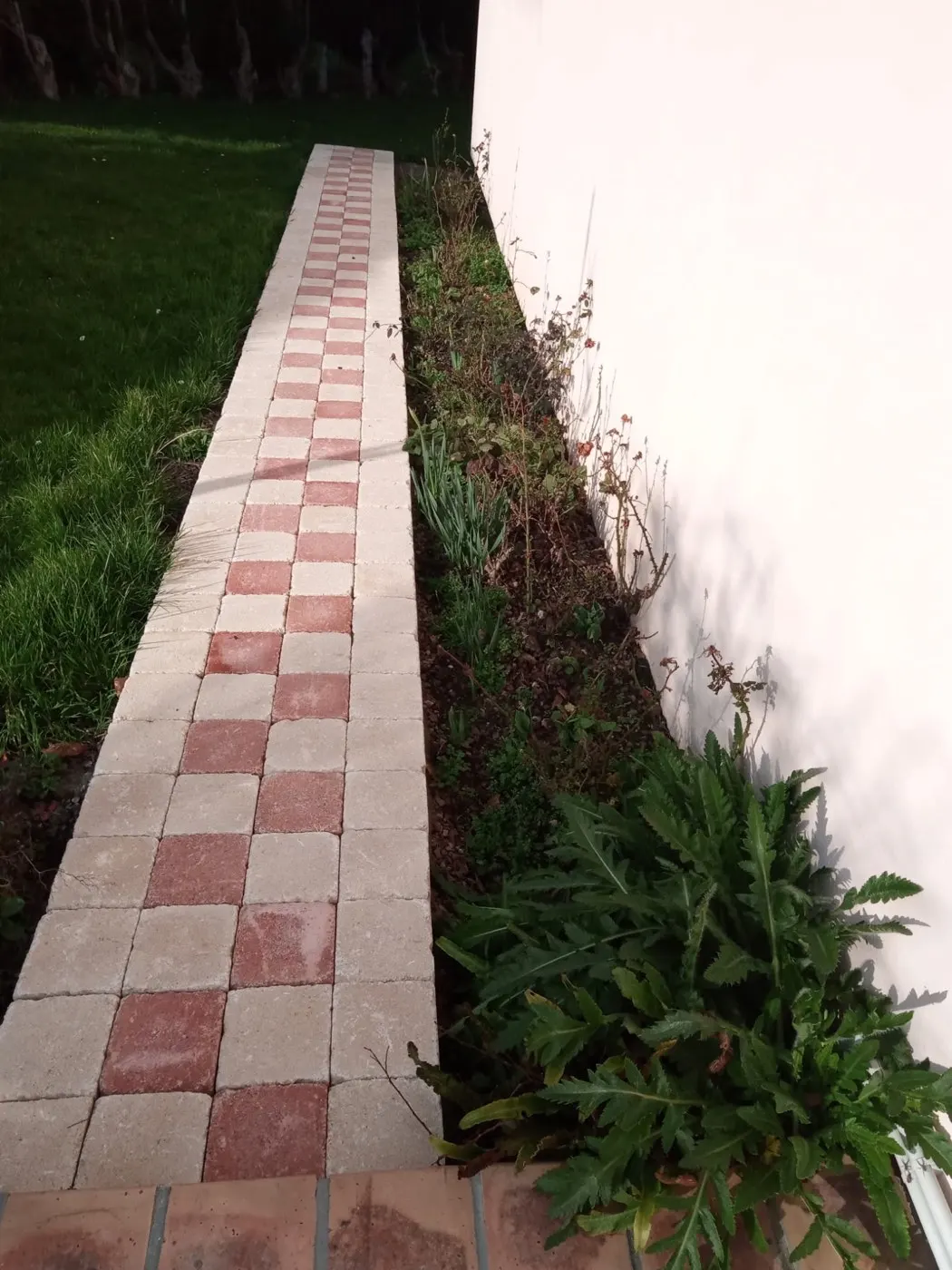 Allée pavée et massif entretenus le long d'une maison, après passage